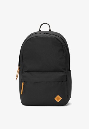 Mochila de tela negra con parte superior redondeada, que cuenta con un bolsillo frontal con cremallera, acentos en color naranja en la cremallera y un parche de logo marrón.