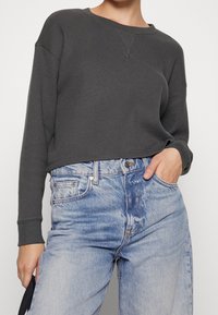 Felpa grigia in tessuto waffle con scollo rotondo e polsini a costine, abbinata a jeans in denim a vita alta di colore blu chiaro con una texture sbiadita.