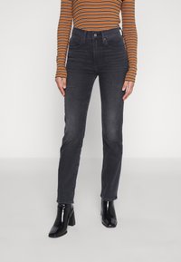 Jeans grigio scuro a vita alta con design aderente e texture liscia, abbinati a una maglia a maniche lunghe a righe e stivali neri lucidi con tacco largo.