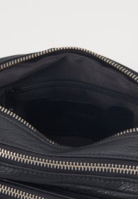 Indvendig på en sort lædertaske med struktureret design, der har en lynlås lomme og synlige sølvlynlås tænder ved åbningen. Tekstureret foring.