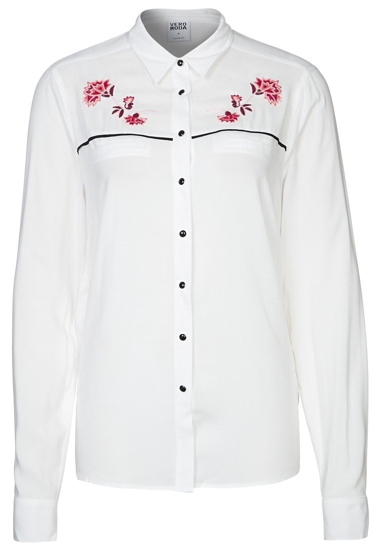 Bílá halenka s dlouhým rukávem, černými knoflíky, předními kapsami a květinovou výšivkou v růžové a červené barvě na ramenou, s klasickým límečkem.