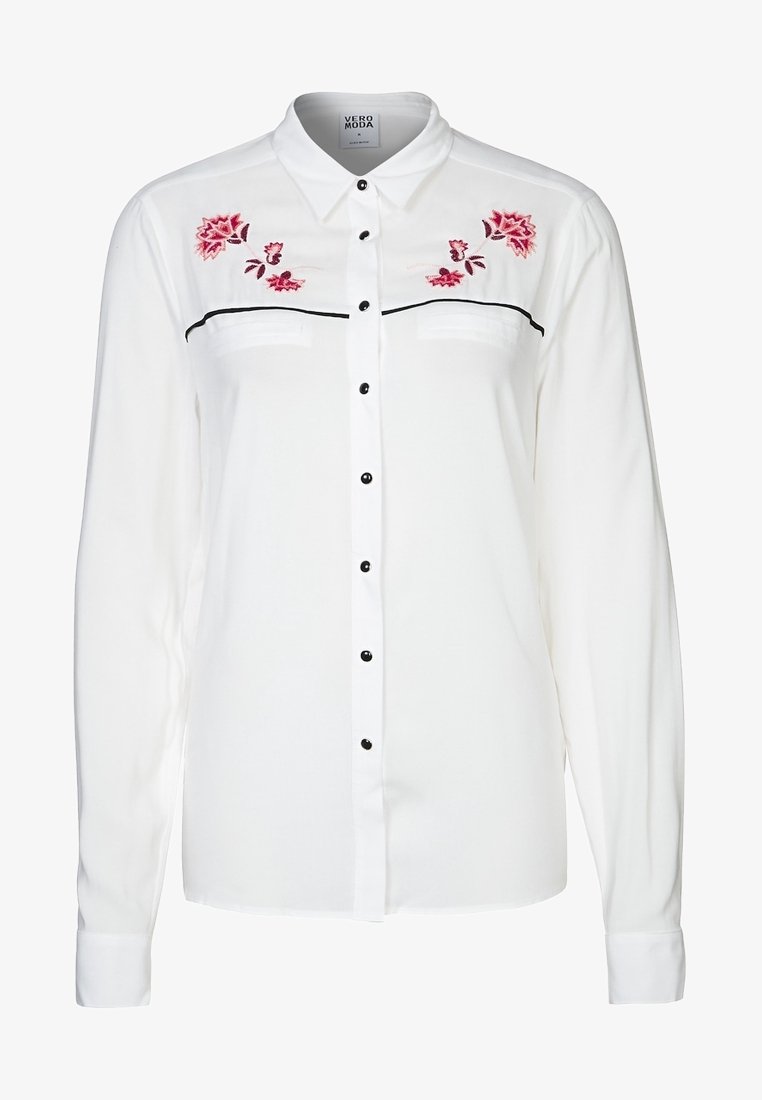 Bílá halenka s dlouhým rukávem, černými knoflíky, předními kapsami a květinovou výšivkou v růžové a červené barvě na ramenou, s klasickým límečkem.