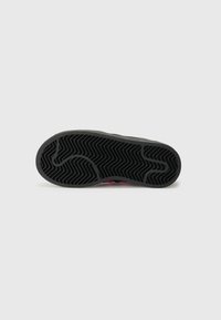 Sålen på en sneakers med en teksturert svart gummioverflate med sikksakkmønstre og en rosa detalj på hælen.
