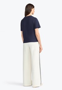 T-shirt bleu marine à manches courtes avec col rond, associé à un pantalon blanc ample avec des rayures noires sur les côtés. Design simple et épuré.