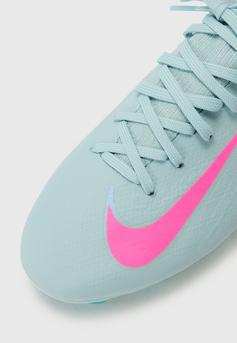 Chaussure de football bleu clair en matériau texturé avec un swoosh Nike rose. Elle présente des lacets fins et plats ainsi qu'un design de orteil arrondi.