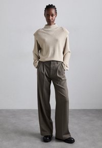 Beige sweater with a high neck and textured detail, paired with high-waisted, wide-leg dark olive trousers, and chunky black shoes.