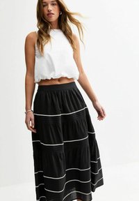 Débardeur blanc court avec un col rond associé à une jupe maxi noire comportant des segments superposés et des accents de couture blanche.