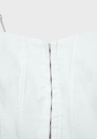Tissu blanc avec coutures verticales et fermeture centrale métallique à crochets et œillets, montrant une partie d'un vêtement supérieur ou d'une robe.