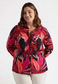 Camisa de botones con fondo negro que presenta vibrantes patrones botánicos en rosa y rojo. Mangas largas, corte ajustado, tejido ligero.