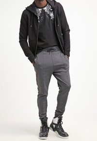 Svart zip-up hoodie, grafisk svart t-shirt, grå tapered sweatpants med fickor, och svart-vita high-top sneakers.
