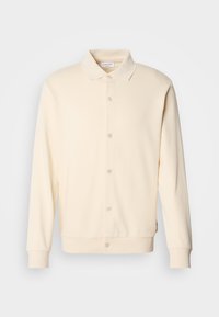 Felpa button-up color crema con maniche lunghe, colletto e polsini a coste. Texture liscia, design minimalista.