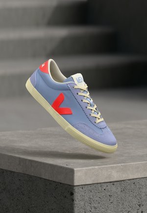 Baskets en cuir bleu clair avec accents rouges contrastants, lacets beiges et semelle texturée. Présente un bout arrondi et un col rembourré.