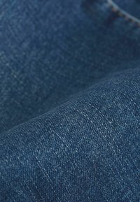 Tumed sinise tooni denim kangas, millel on tekstureeritud pind, näidates ühtlast kootud mustrit ja õrnu värvi varieerumise. 