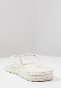 Witte espadrille flip-flop met dikke geweven zool en glanzende banden, met een textuur op het oppervlak en een afgeronde teenontwerp.