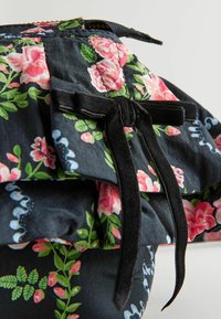 Blommönstrad tygkjol i mörk marinblå, med rosa rosor och gröna blad, lagerdesign med en svart sammetssnörning i midjan.