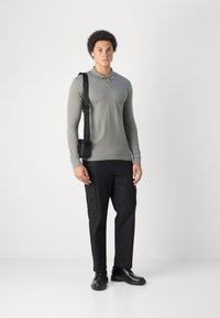 Lange mouwen, lichtgrijze polo met een kraag; gecombineerd met zwarte cargobroeken met zijzakken en zwarte veterschoenen. Zwarte schoudertas.