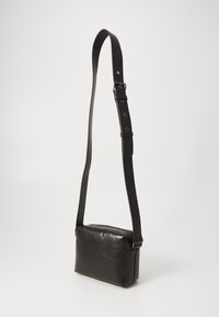 Čierna kožená crossbody taška s obdĺžnikovým tvarom, nastaviteľným popruhom a jemným leskom. Zips na vrchu. Jednoduchý, minimalistický dizajn.