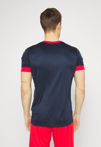 Marineblaues Sport-T-Shirt mit roten Akzenten an den Ärmeln und am Kragen; aus glattem, dehnbarem Stoff gefertigt. Die Rückansicht zeigt ein minimalistisches Design und eine schicke Passform.