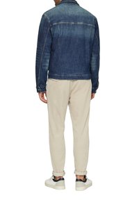Dunkelblaue Jeansjacke mit einem verblassten Effekt, die über zwei hinteren Taschen, Knopfmanschetten und einem klassischen Kragen verfügt. Getragen über hellen Hosen.