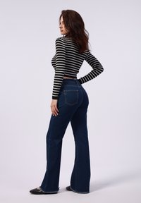 Zwart-wit gestreepte cropped trui, donkerblauwe flared jeans en zwarte ballerina's. De jeans hebben een achterzak en een gehaakte zoom.