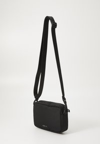 Black crossbody bag made of textured fabric, rectangular shape, featuring a zip closure, adjustable strap, and a logo on the front.