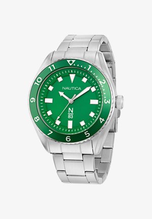 Roheline kell roostevabast terasest rihmaga, suured valged tunni numbrid ja hõbedased käed. Ümar korpus, bezel numbritega, bränd "Nautica" on nähtav.