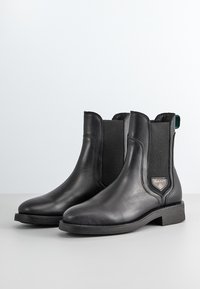 Schwarze Leder-Ankle-Boots mit elastischen Seitenpanelen, niedrigen Absätzen und einem kleinen GANT-Logo-Patch an der Außenseite jedes Boots.
