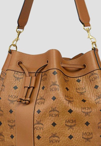 Sac seau en cuir fauve avec logos MCM noirs et formes losanges, doté d'une fermeture à cordon de serrage et d'une bandoulière réglable avec ferrures dorées.