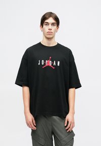 Crna pamučna majica s oversized krojem, s bijelim i crvenim "JORDAN" logotipom i siluetom na prsima. Kratki rukavi, okrugli izrez.