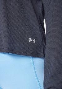 Top atlético de color azul oscuro con una textura sutil, que presenta un logo plateado en el dobladillo, combinado con un pantalón ajustado de color azul claro.