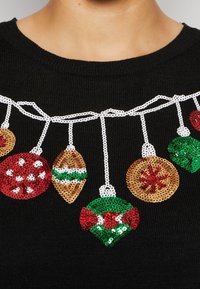 Black sweater featuring a sequin Christmas ornament design in red, green, gold, and white. Ornaments vary in shape and detail.