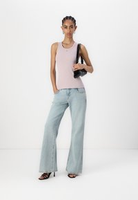 Lys rosa tettsittende tank topp med en liten logo, matchende vide lyseblå jeans og svarte høyhælte sandaler. Svart håndveske som aksent.