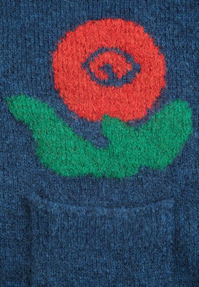 Fleur rouge avec des feuilles vertes tricotée sur un tissu en laine bleu foncé, au-dessus d'une petite poche.