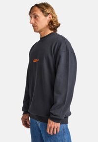 Sudadera gris oscuro hecha de una mezcla de algodón, con un cuello acanalado, un sutil logo naranja en el pecho y un corte relajado.