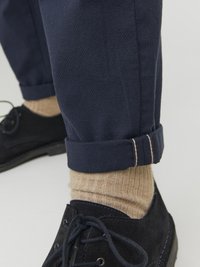 Marineblaue Hose mit strukturiertem Muster, umgeschlagenen Säumen, kombiniert mit dunkelbraunen Wildlederschuhen und hellbeigen gerippten Socken.