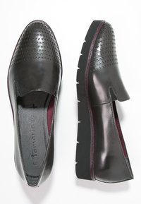 Scarpe slip-on nere perforate con punta tonda, parte superiore texturizzata e suola nera spessa con un accento maroon discreto lungo il bordo.