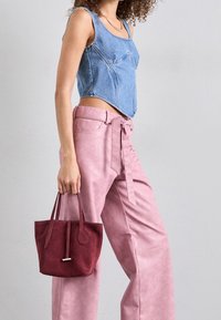Denim crop top med en figursydd design, matchad med högmidjade byxor i rosa konstläder. Modellen håller en liten handväska i burgundy mocka.