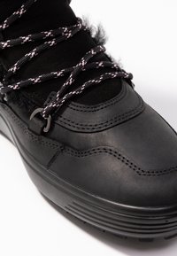 Bottine en cuir noir à surface texturée, avec des lacets à motif rose et noir, et une semelle extérieure en caoutchouc avec des rainures horizontales.