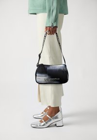 Borsa stampata in bianco e nero con forma arrotondata, dotata di una tracolla e il nome "KARL LAGERFELD" in testo argentato.