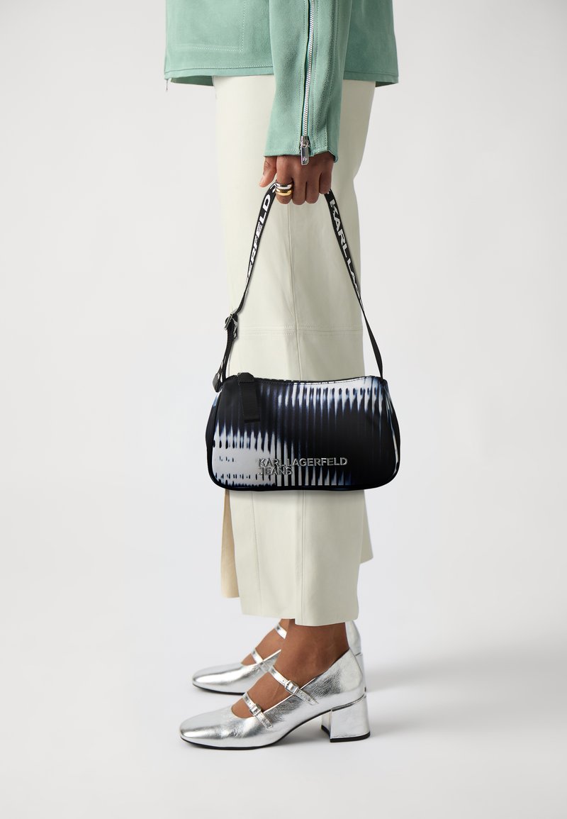 Borsa stampata in bianco e nero con forma arrotondata, dotata di una tracolla e il nome "KARL LAGERFELD" in testo argentato.