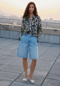 Camicia a bottoni con stampa leopardata, pantaloni corti in denim azzurro, tacchi bianchi aperti. Tessuto strutturato e pantaloni corti dalla vestibilità rilassata con vita classica.