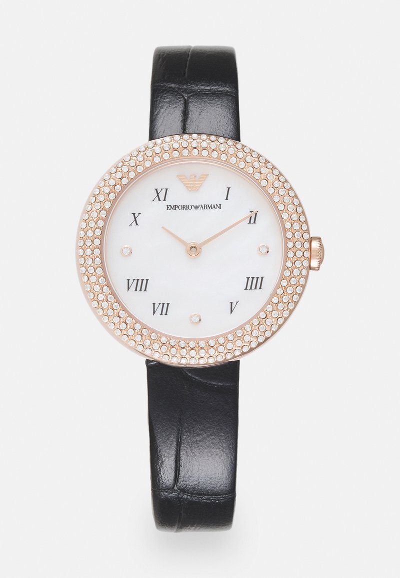Montre ronde avec un cadran en nacre blanche, un boîtier en acier rose orné de cristaux, un bracelet en cuir noir et des chiffres romains.