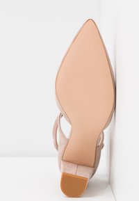 Chaussure à talon haut en daim beige avec un bout pointu et un talon carré, dotée d'une semelle extérieure en caoutchouc texturé pour l'adhérence.