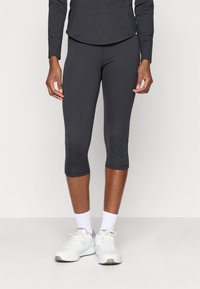 Leggings recortados negros de tela elástica, con una textura suave y un ajuste ceñido, combinados con zapatillas deportivas blancas y calcetines.