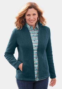 Türkiser Fleece-Jacke mit hohem Kragen, ausgestattet mit einem Reißverschluss und seitlichen Taschen. Getragen über einem blau-grünen Karoshirt.