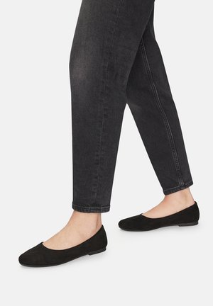 Bailarinas de ante negro con punta redondeada y suela plana, combinadas con jeans negros arremangados. Superficie texturizada visible en los materiales del zapato.