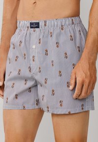 Boxer in cotone con righe verticali blu e bianche, caratterizzati da piccole illustrazioni a motivo di soldatini, fascia elastica in vita e pattina con bottone.