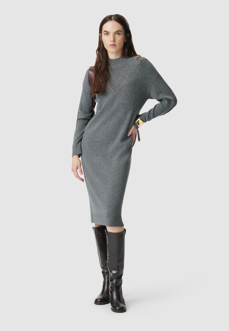 Szara dzianinowa sukienka z długim rękawem, z prążkowanymi mankietami i dołem. Połączona z czarnymi skórzanymi botkami za kolano i brązową skórzaną torbą na ramię.