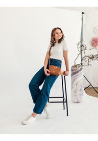 Braune strukturierte Umhängetasche mit einer Kettenriemen, getragen über einem weißen eng anliegenden Oberteil und hochtaillierten blauen Jeans, kombiniert mit weißen Sneakers.
