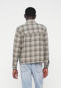 Koszula z flaneli w kratę w stonowanych odcieniach szarości z kontrastującymi białymi i beżowymi liniami, wyposażona w kołnierzyk i mankiety na guziki.